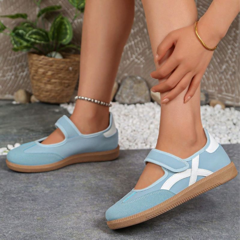 Blue women's Mary Jane trainers with white curved stripes, side view on feet