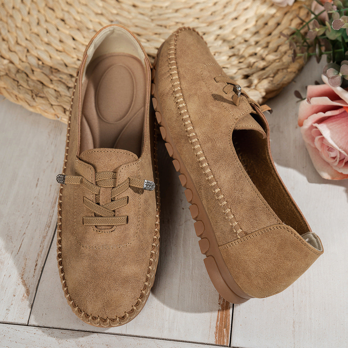 Tan women's suede loafers showing the shaped insole and stitched side profile beside flowers