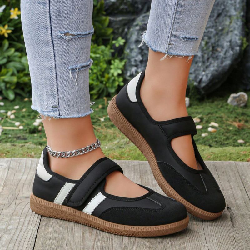 Black and white women's Mary Jane trainers with adjustable straps, close-up on feet