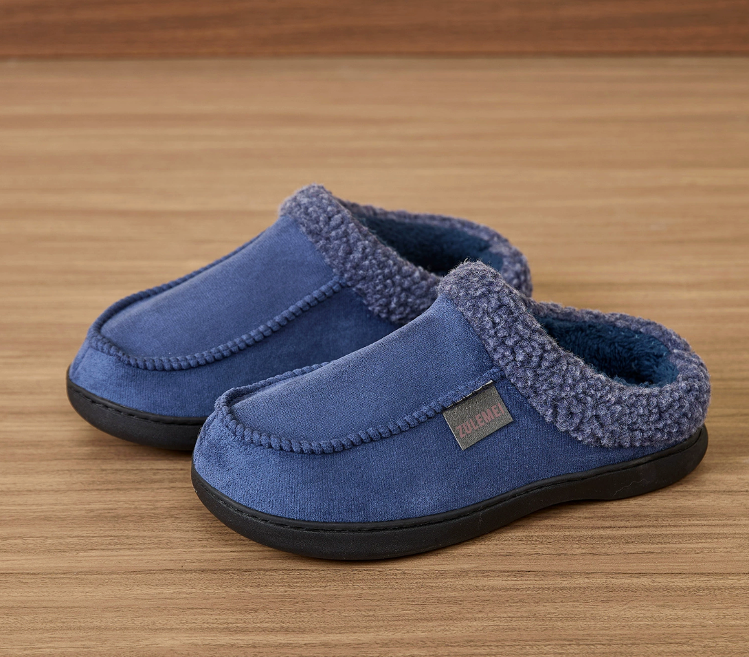 Auldweave Men’s warm wide fit winter slippers. Pair of blue slippers with fuzzy trim on a wooden surface