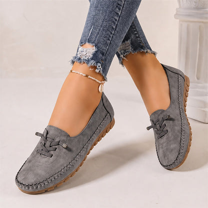 Dark grey women's suede slip-on loafers with rounded toes, angled view on feet