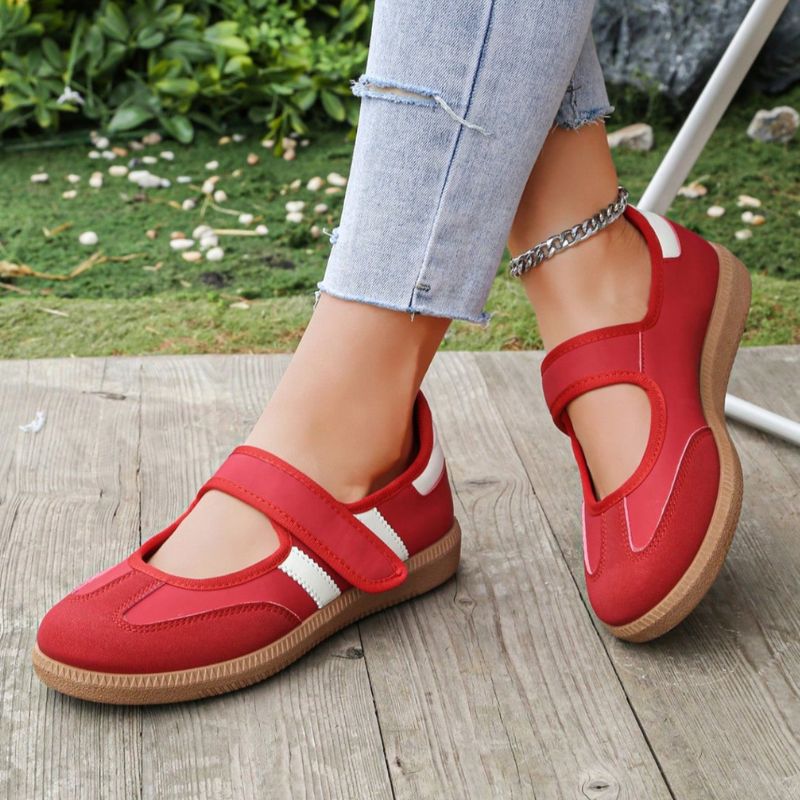 Red women's Mary Jane trainers with white side stripes, angled view on feet