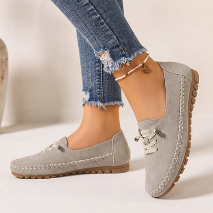 Light grey women's wide fit suede loafers with brown soles, side view on feet