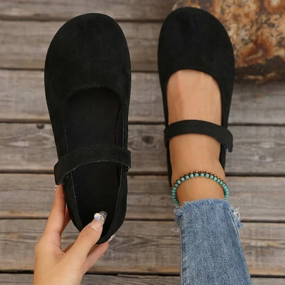 Women's black Mary Jane flats shown on foot with one shoe held