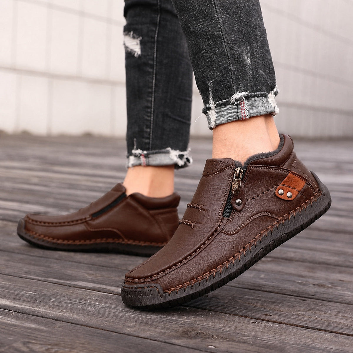 Dark brown men's zip-up leather ankle boots with decorative straps, worn with jeans