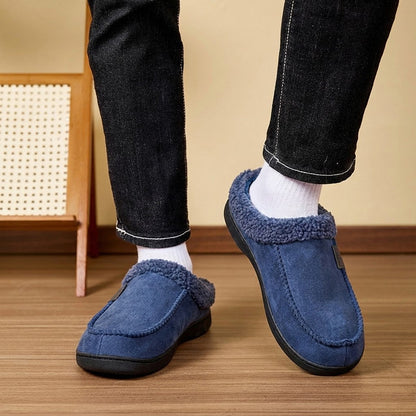 Auldweave Men’s warm wide fit winter slippers. Person wearing blue slippers with fuzzy trim on a wooden floor.