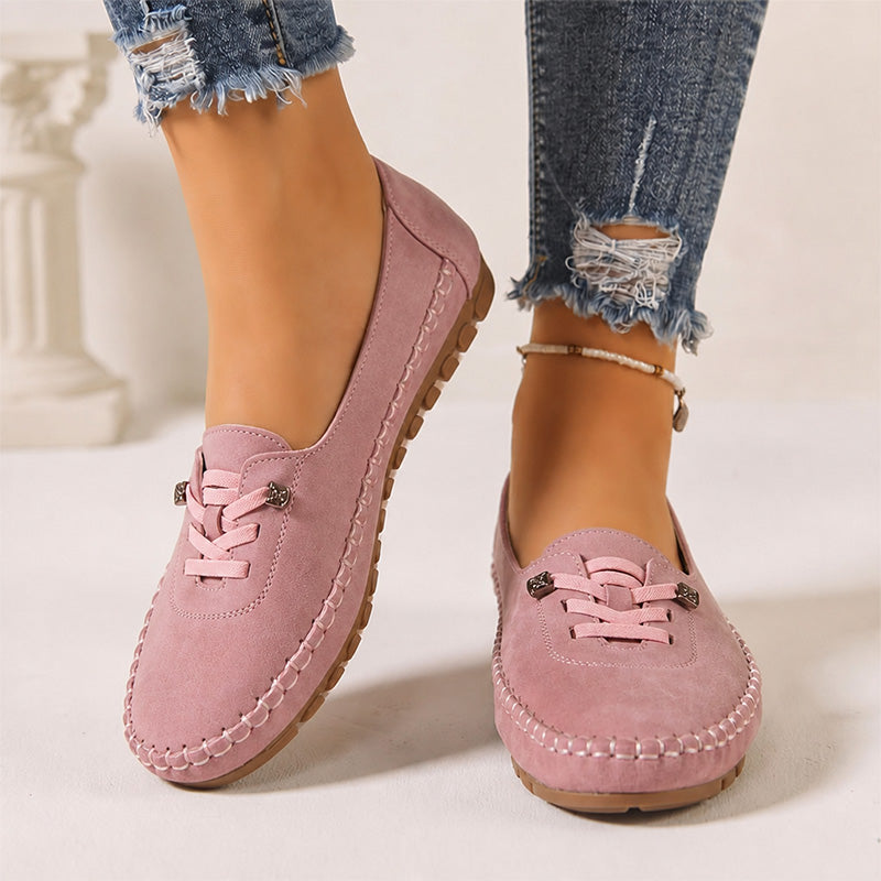 Pink women's suede slip-on loafers with stitched edges, front view on feet