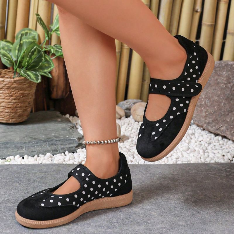 Black polka-dot women's Mary Jane trainers with gum soles, angled side view on feet