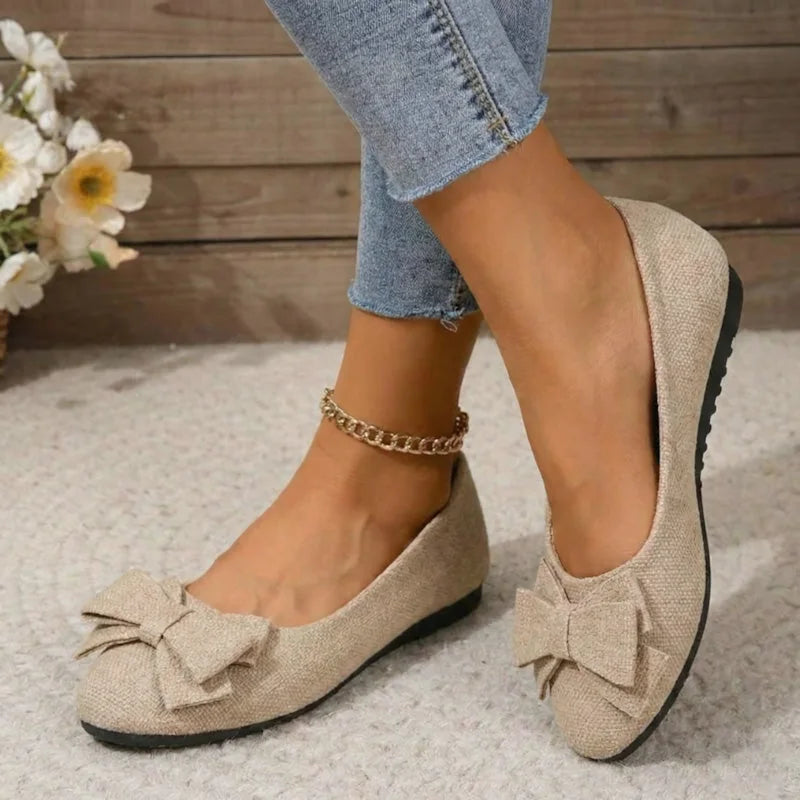 Beige bow ballet flats worn with jeans, angled view