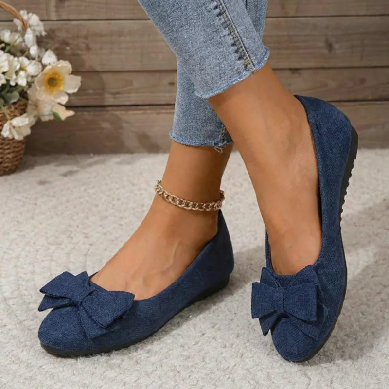 Navy blue bow ballet flats worn with jeans, angled view